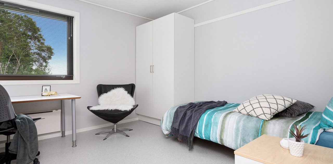 Romslige private soverom med 90-seng, klesskap, nattbord, skrivebord med arbeisstol, bokhylle og lenestol. ©StudioIstad