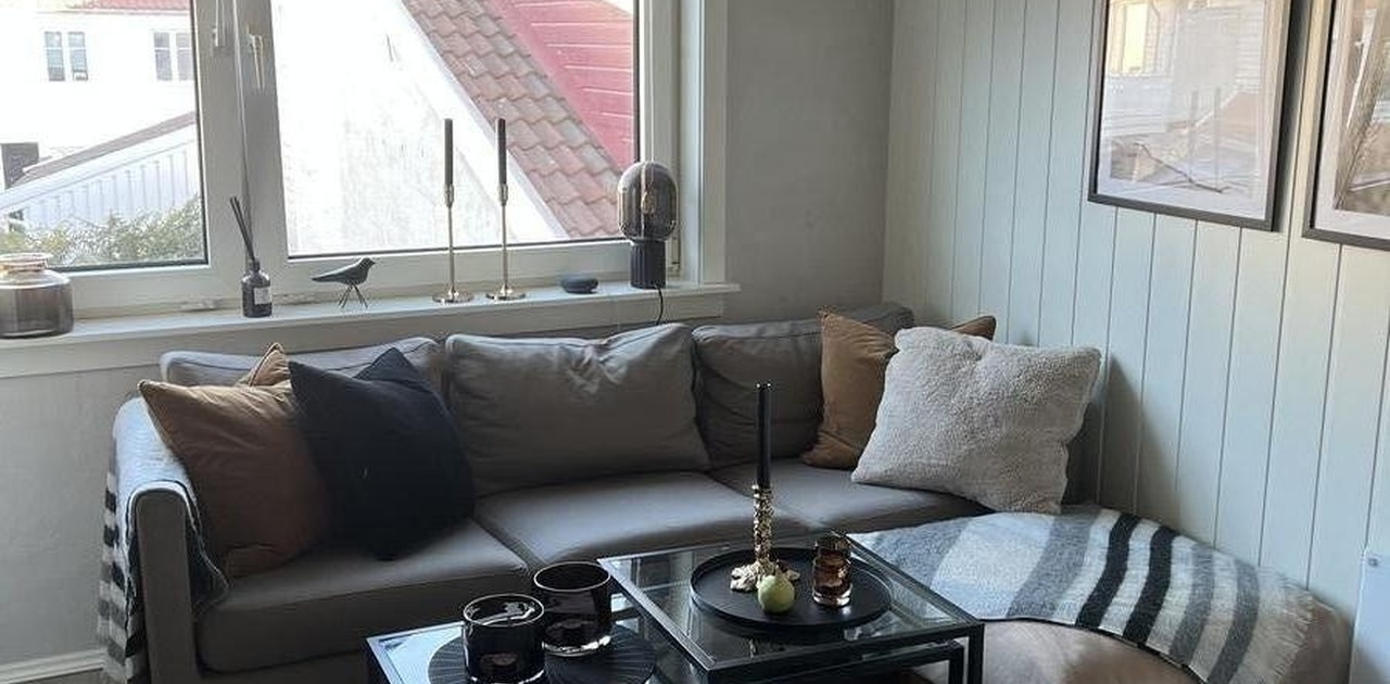 Koselig stue med sofagruppe og store vinduer vendt mot bakgården.